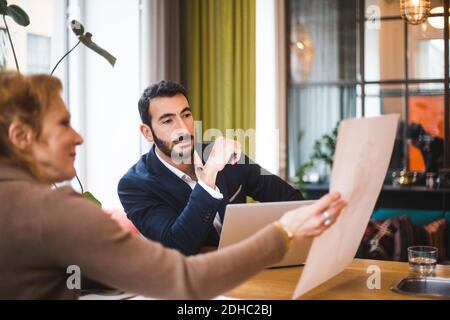 Confident male and female professionals discussing over drawing on paper at table in office Stock Photo