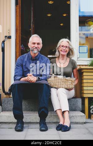 Portrait of male and female colleagues sitting on steps at store entrance Stock Photo