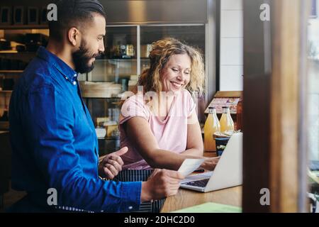 Colleagues smiling with discussing over laptop at table in deli Stock Photo