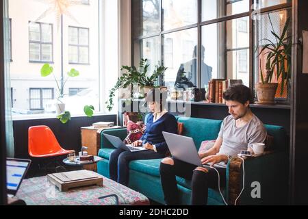 Multi-ethnic male and female professionals using laptops sitting on sofa at office Stock Photo