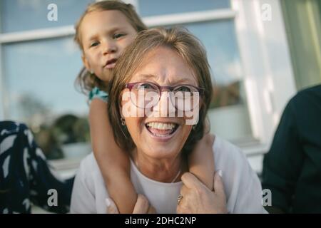 Happy senior woman piggybacking granddaughter at porch Stock Photo