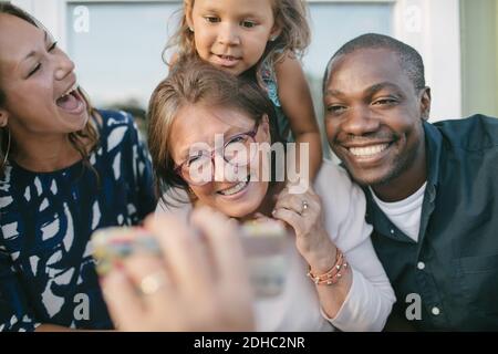 Cropped image of man showing mobile phone to happy family on porch Stock Photo