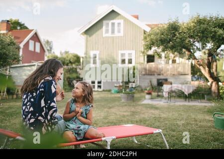 Smiling mother and daughter talking while sitting on lounge chair in backyard Stock Photo