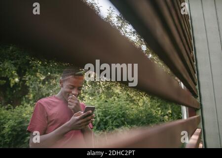 Smiling boy using mobile phone seen through fence in backyard Stock Photo