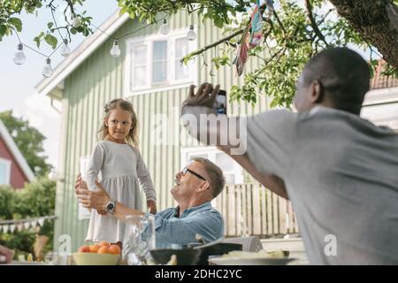Male photographing daughter standing by senior man at table during garden party Stock Photo