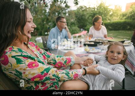 Cheerful mother holding hands of daughter while sitting on chair during garden party Stock Photo