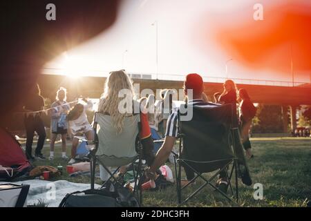 Rear view of man and woman holding hands while sitting on chairs in music festival Stock Photo