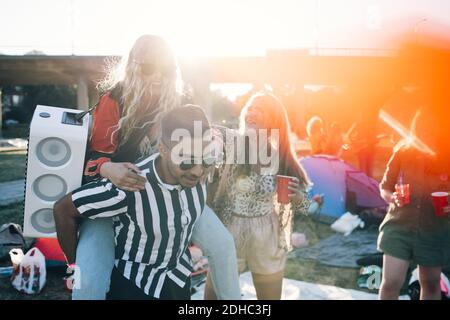 Man piggybacking female friend with speaker while enjoying in music festival Stock Photo