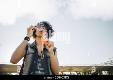 Low angle view of young man blowing soap bubbles against sky Stock Photo