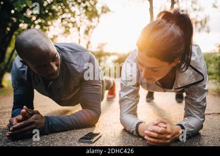 Male and female athletes looking at mobile phone while doing planks on road in park Stock Photo