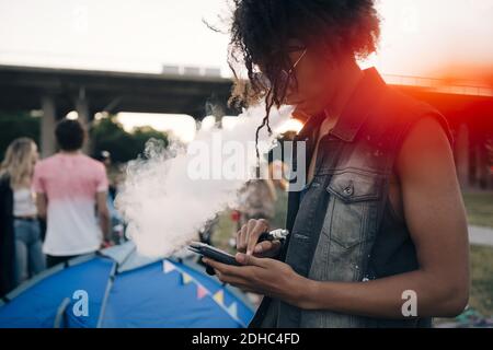 Side view of young man smoking while using mobile phone at music event Stock Photo