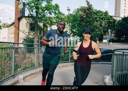 Determined male and female friends jogging on bridge in city Stock Photo