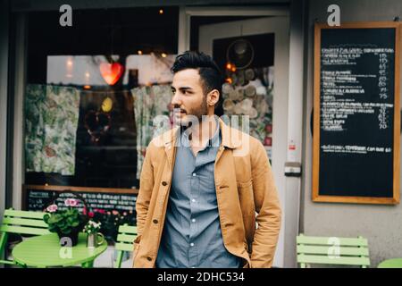 Thoughtful young man looking away while standing against restaurant Stock Photo