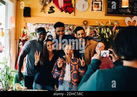 Young man photographing cheerful multi-ethnic friends standing at restaurant during brunch Stock Photo
