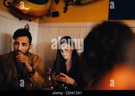 Young woman using smart phone while sitting by man in restaurant Stock Photo