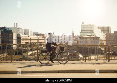 Full length side view of young man riding electric bicycle on bridge in city Stock Photo