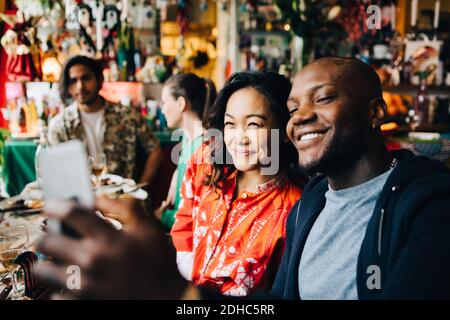 Smiling young man taking selfie with friend while sitting at table in restaurant Stock Photo