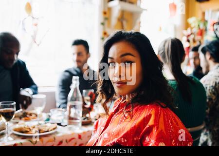 Portrait of confident young woman sitting at table against multi-ethnic friends enjoying brunch in restaurant Stock Photo