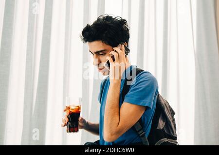 Young man answering smart phone while holding cola in restaurant Stock Photo