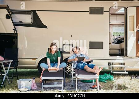 Teenage siblings watching movie on digital tablet while sitting on folding chairs against motor home at campsite Stock Photo