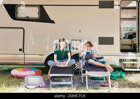 Brother and sister using digital tablet while sitting on folding chairs against motor home Stock Photo