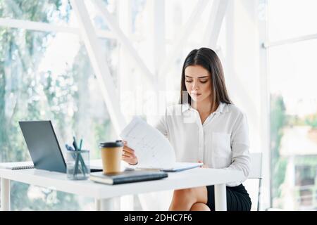 Pretty businesswoman sitting at workplace and reading documents in her modern office Stock Photo