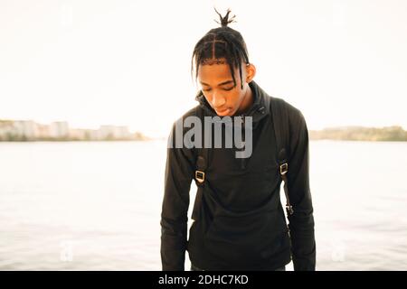 Teenage boy looking down while standing against river Stock Photo