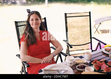 Thoughtful smiling woman sitting at table on folding chair at campsite Stock Photo