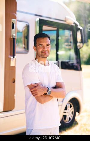 Portrait of confident mature man standing with arms crossed by travel trailer Stock Photo