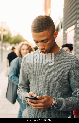 Teenage boy using mobile phone while standing on street in city Stock Photo