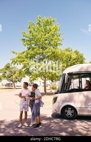 Father and children reading map while woman sitting in camper trailer at park Stock Photo