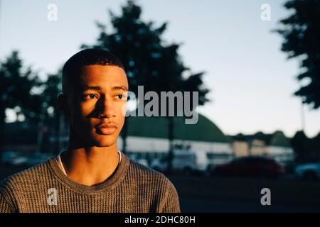 Thoughtful teenage boy looking away in city during sunset Stock Photo