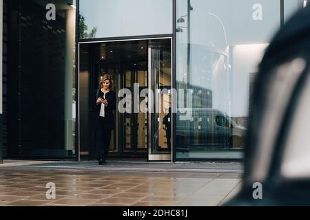 Full length of businesswoman using smart phone while leaving from office Stock Photo