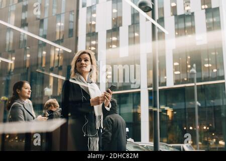 Low angle view of businesswomen using smart phones while standing against modern building in city Stock Photo