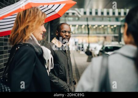 Colleagues talking while standing on sidewalk in city Stock Photo