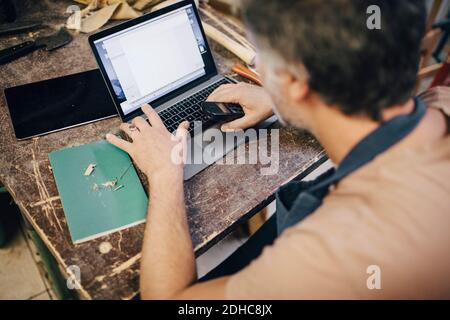 High angle view of male craftsperson using laptop at workbench in workshop Stock Photo