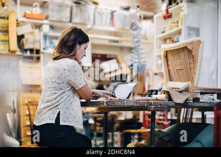 Female upholstery worker using laptop at workbench in workshop Stock Photo