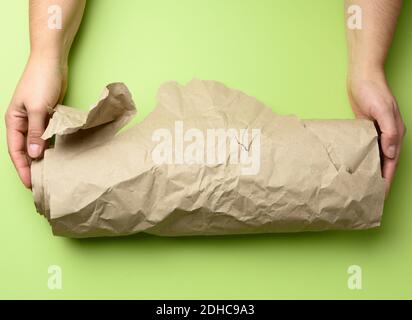 Two female hands hold rolled brown paper, green background Stock Photo