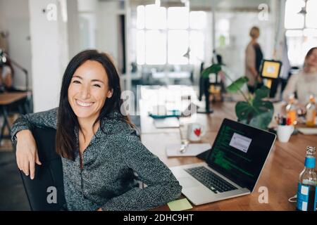 Portrait of smiling female computer programmer sitting at desk in creative office Stock Photo