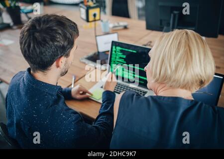 Male and female computer programmers discussing over laptop at desk in creative office Stock Photo