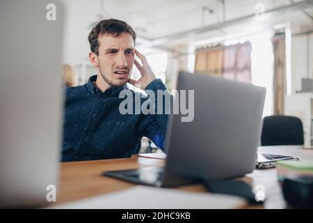 Confused businessman looking at laptop while sitting at desk in office Stock Photo