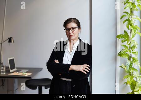 Portrait of confident mature businesswoman leaning on wall in office Stock Photo