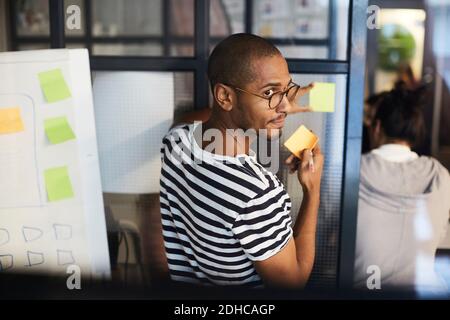 Creative businessman sticking adhesive note on glass in office Stock Photo