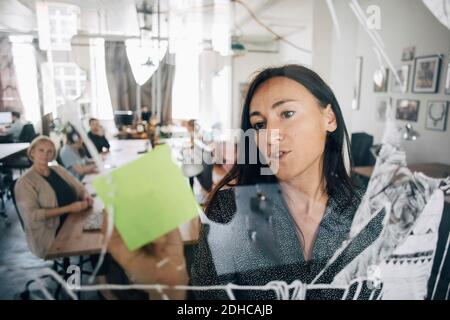 Businesswoman writing on sticky note while explaining colleagues during meeting in creative office Stock Photo
