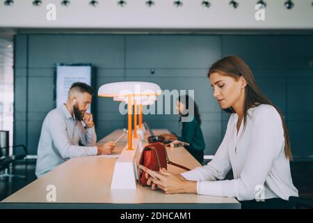 Young businesswoman using smart phone while sitting with multi-ethnic colleagues at table waiting in airport departure a Stock Photo