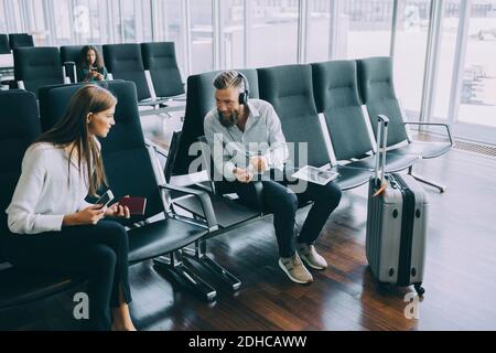 Smiling businessman talking to businesswoman while sitting at waiting room in airport Stock Photo