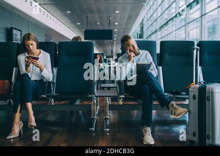 Thoughtful businessman looking away while sitting by female colleague at waiting area in airport Stock Photo