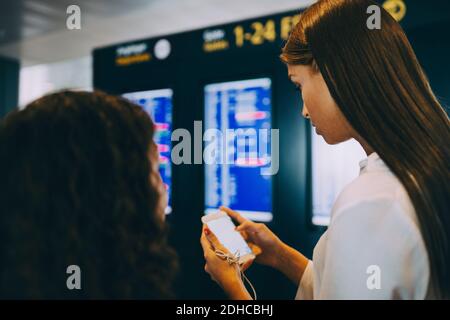 Young businesswoman checking flight timings through smart phone at airport Stock Photo