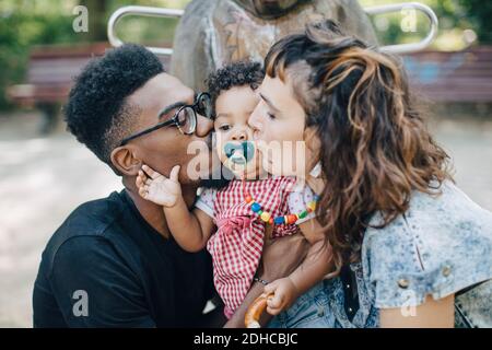 Mother and father kissing daughter sucking pacifier at playground Stock Photo