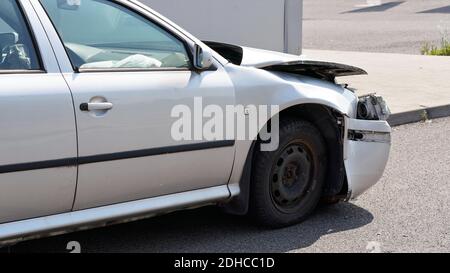 Crashed car standing on road next to curb, side view with demolished front and used airbag inside visible Stock Photo